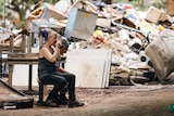 an exhausted woman sits next to piles of rubbish