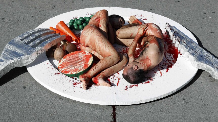 Protestors covered in blood pose on a giant dinner plate