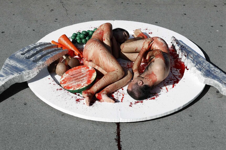 Protestors covered in blood pose on a giant dinner plate
