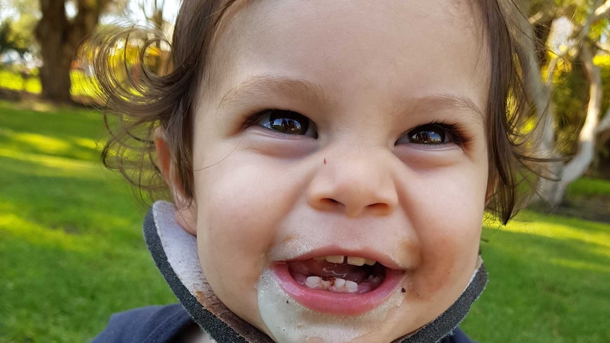 Toddler sits in park smiling