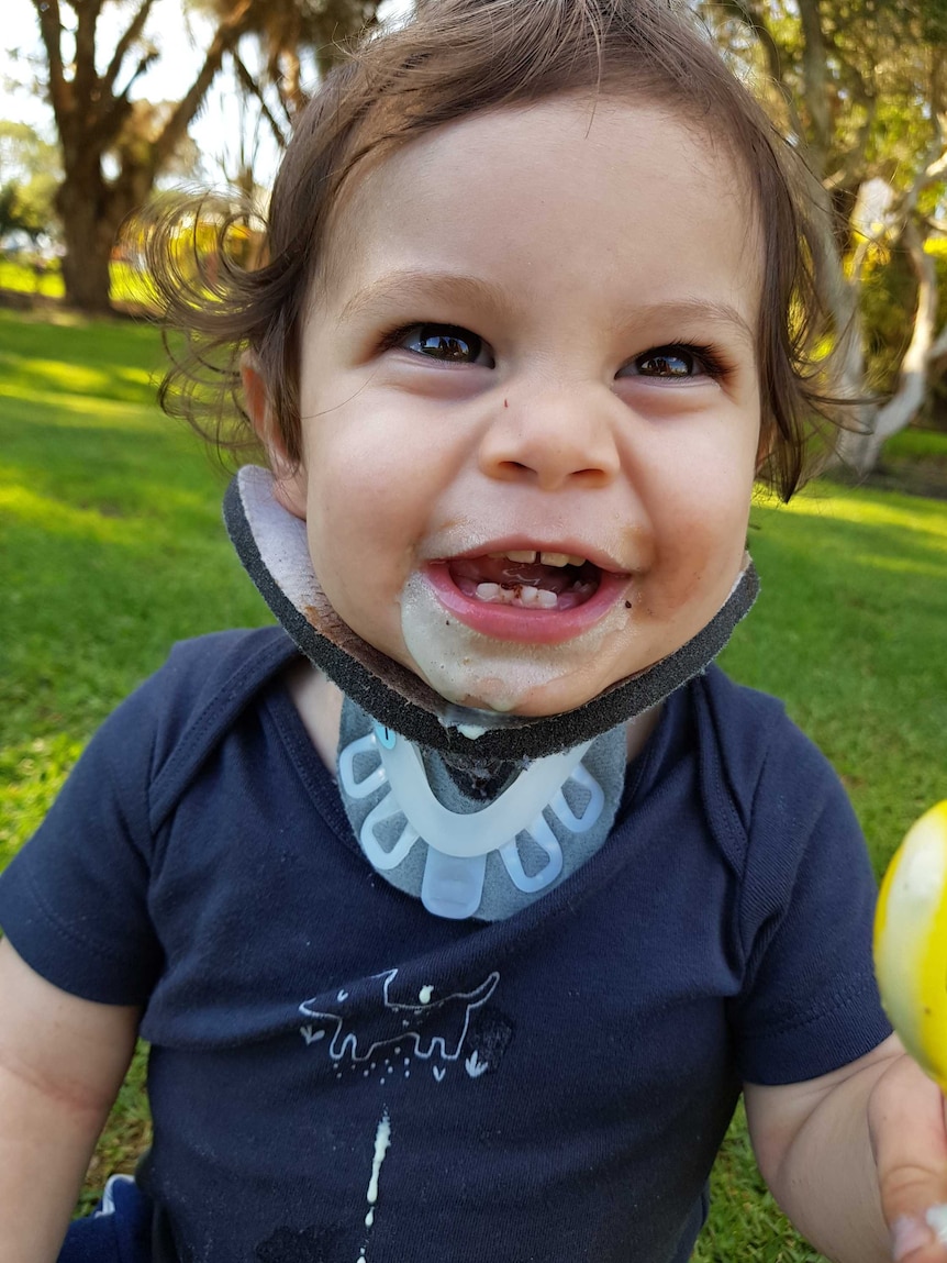 Toddler sits in park smiling