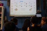 a smartboard with icons on it and a warning sign and children looking on
