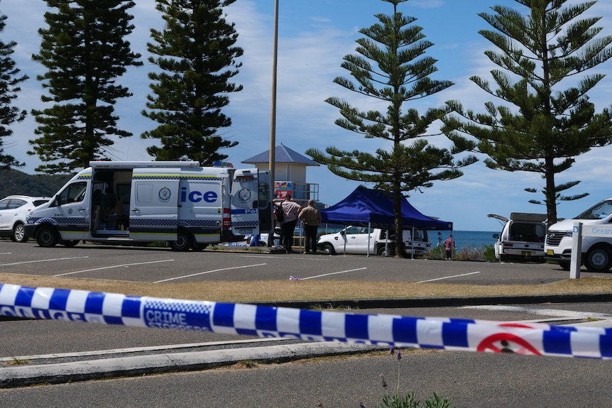 A police van and blue gazebo behind a car park and police tape.