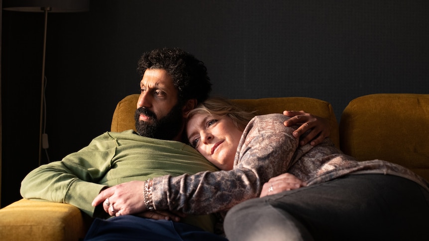 A man and a women hugging each other on a couch looking out a window