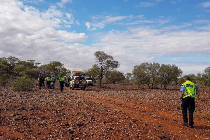 red dirt and some scrub with a few police officers in high vis vests and parked 4WDs