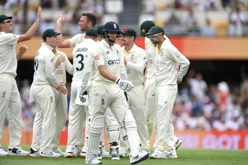 An England batsman trudges off the Gabba after getting out while in the background Australian cricketers celebrate.