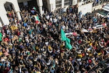 Crowds of people block a street filled with people as they carry bodies on stretchers wrapped in Palestinian flags. 
