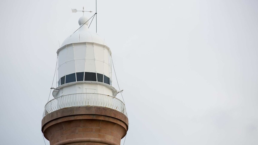 The white top of the lighthouse is seen against an as-white sky.