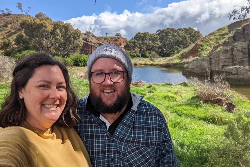 a man and woman smile in front of a lake. 