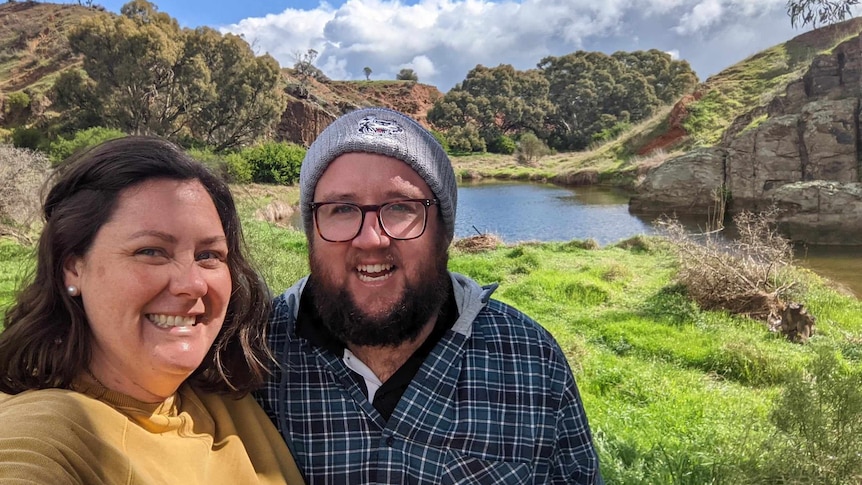 a man and woman smile in front of a lake. 