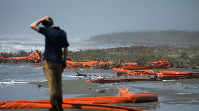 A man stands beside oil booms on a beach after the Gulf of Mexico oil spill disaster.