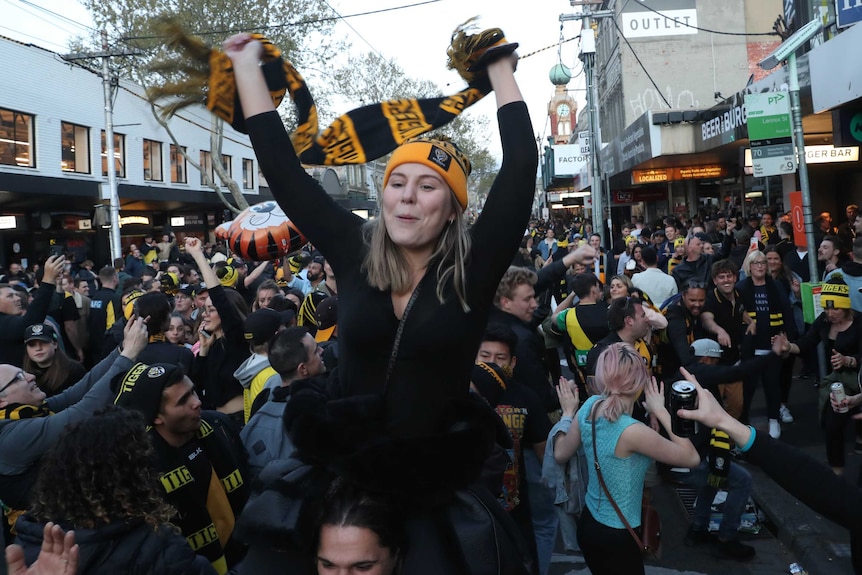 a girl raises a richmond scarf as tigers fans celebrate behind her.