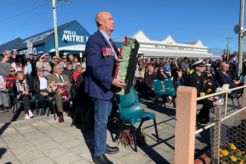 A balding man stands with a wreath