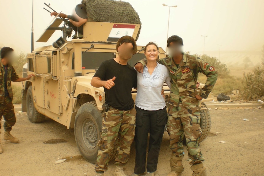 Two soldiers and Andrea stand posing for a photo in front of an armed military vehicle.