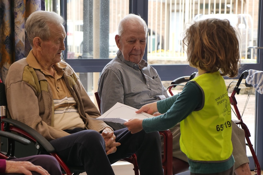 A young boy hands a drawer to an older man at an aged care home.