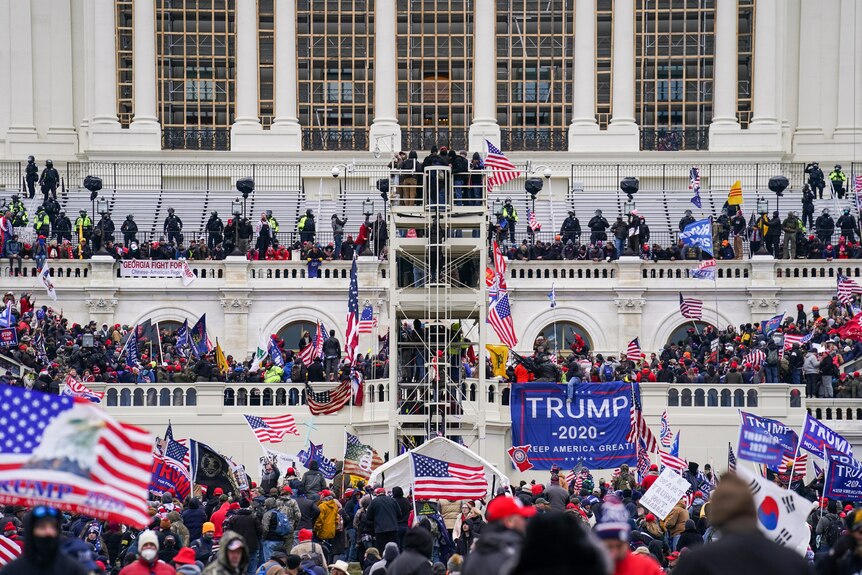 A crowd of people, holding American flags and Trump banners, climb on the Capitol building.