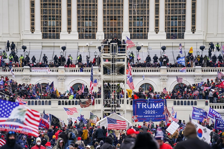 A crowd of people, holding American flags and Trump banners, climb on the Capitol building.