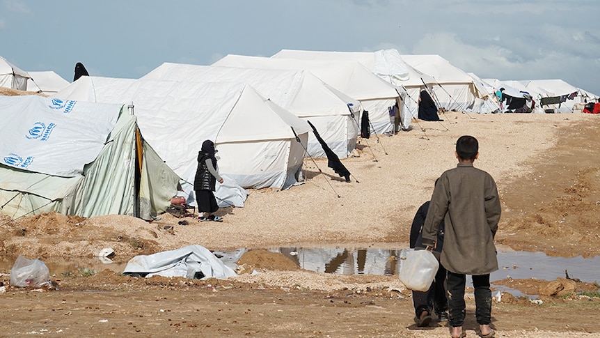 Two boys hold a water container looking over the camp.