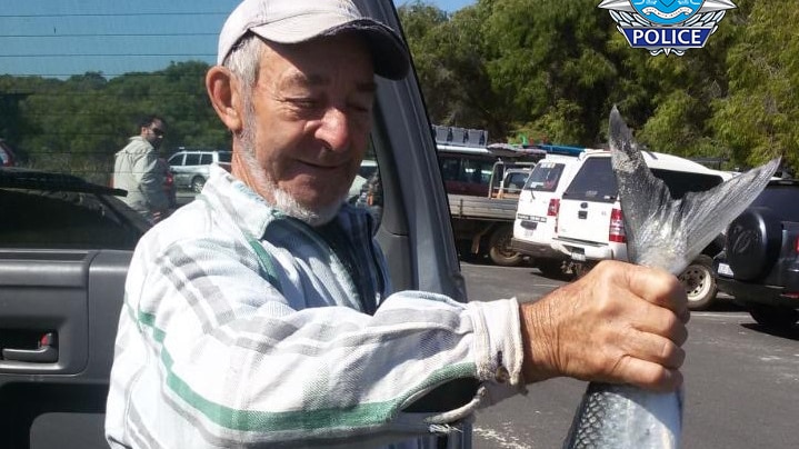 A man standing next to a car holding a large fish by the tail. 