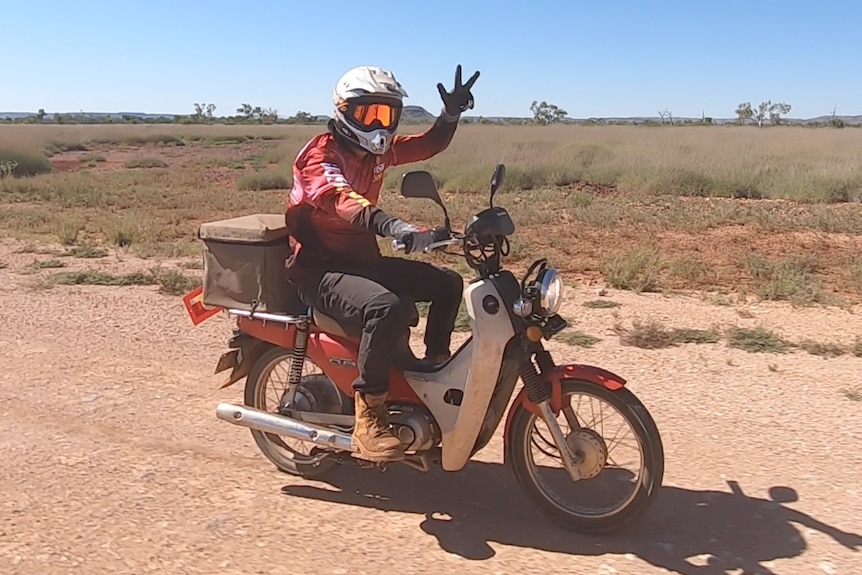 A man, riding a postie bike, on a dirt road in WA's Pilbara