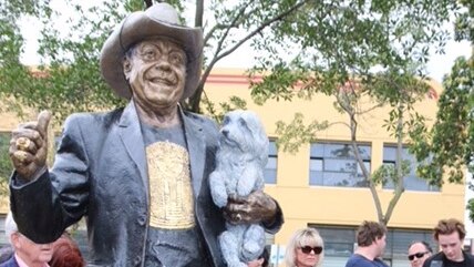 Molly Meldrum sits to the right of the bronze statue made in his honour.