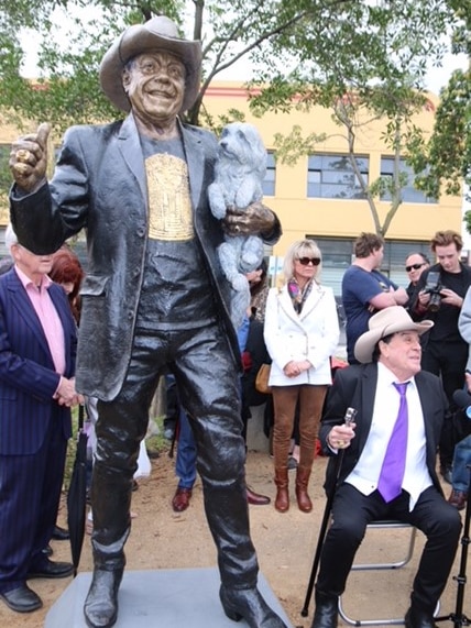 Molly Meldrum sits to the right of the bronze statue made in his honour.