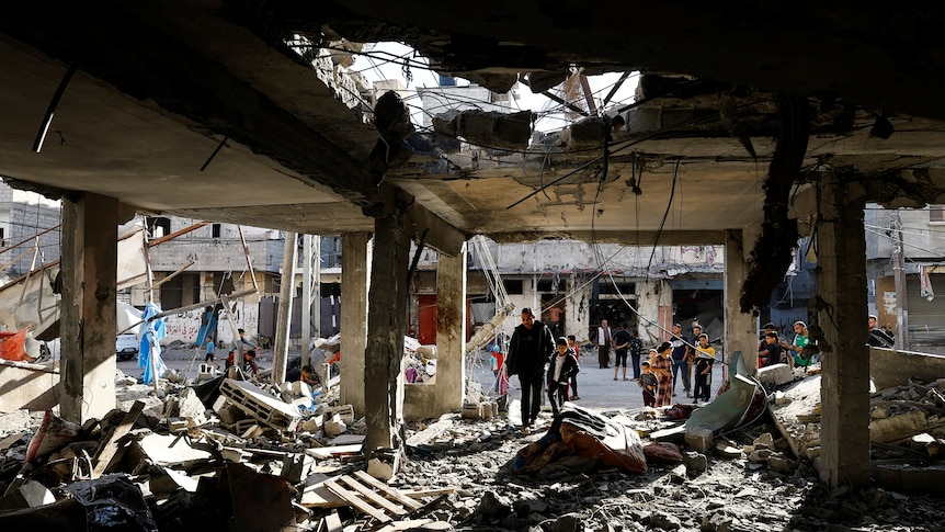 People walk through the bombed-out remains of a house