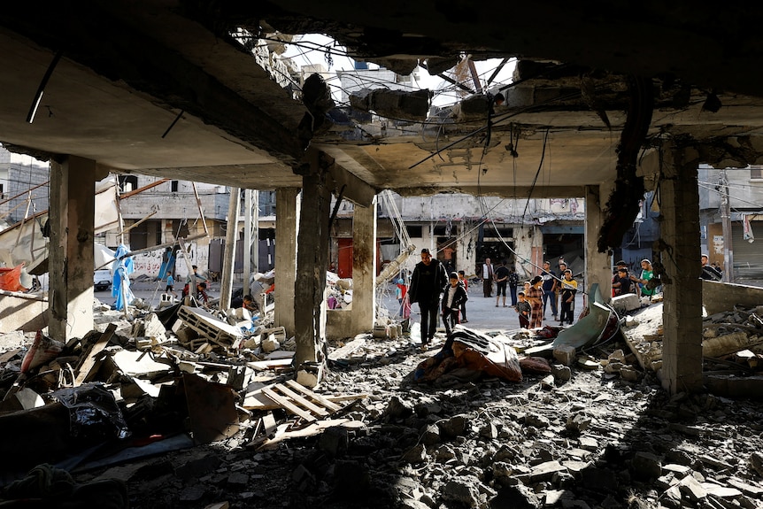 People walk through the bombed-out remains of a house