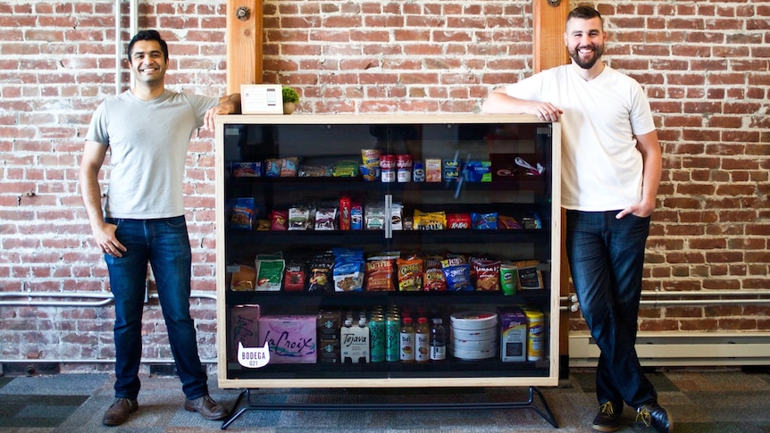 Two men lean on a cabinet that stocks products for sale
