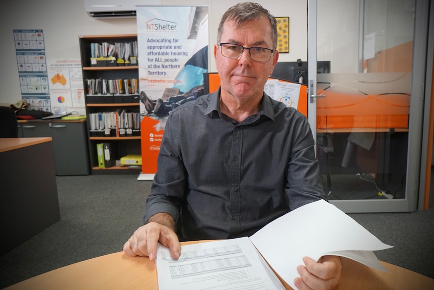 A man sits at a table wearing glasses with papers in front of him