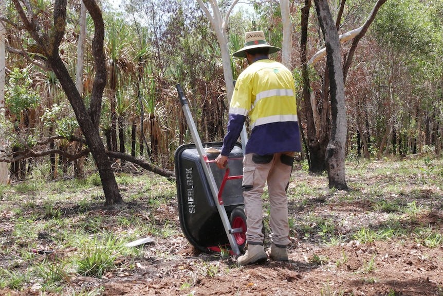 A man wearing a hat and fluorescent work wear empties a wheelbarrow. 