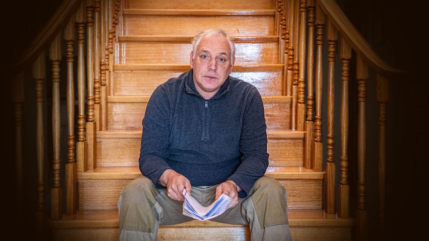 Middle aged man sitting at base of wooden staircase.