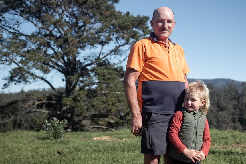 An elderly man in a high vis shirt standing beside a young boy