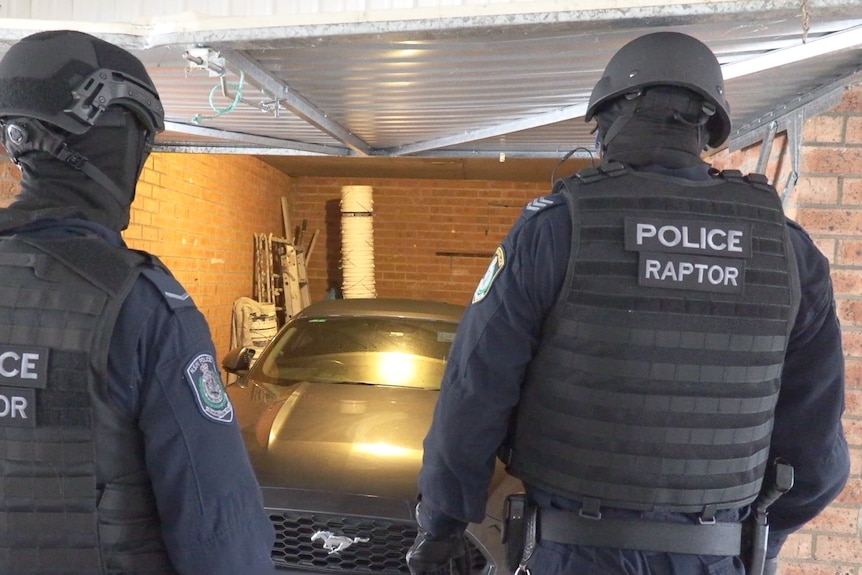 Two armored officers stand in front of a car in a garage