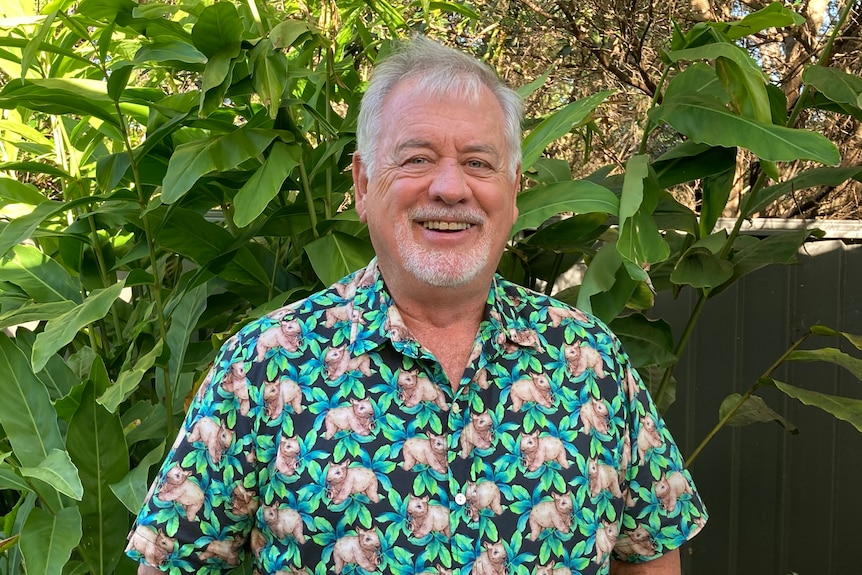 An image of Ken standing in front of greenery 