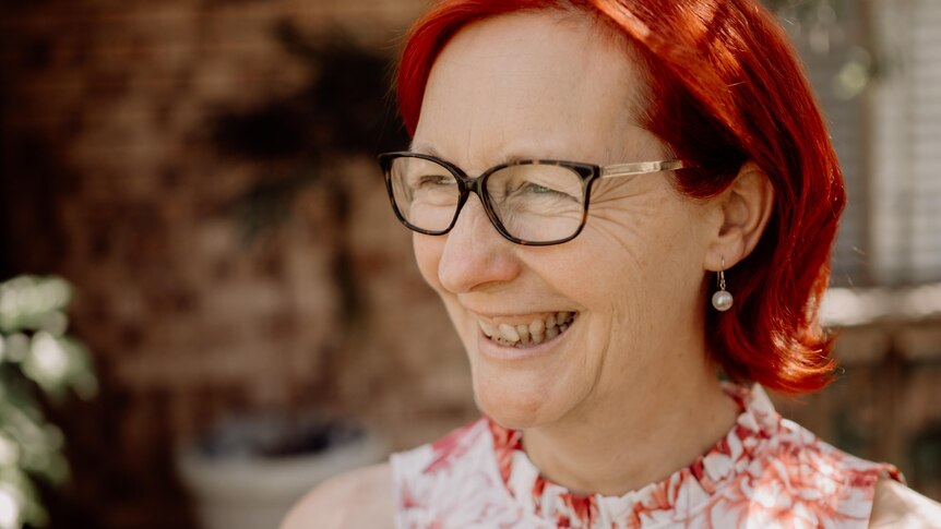 Woman with red hair and glasses smiles in a garden