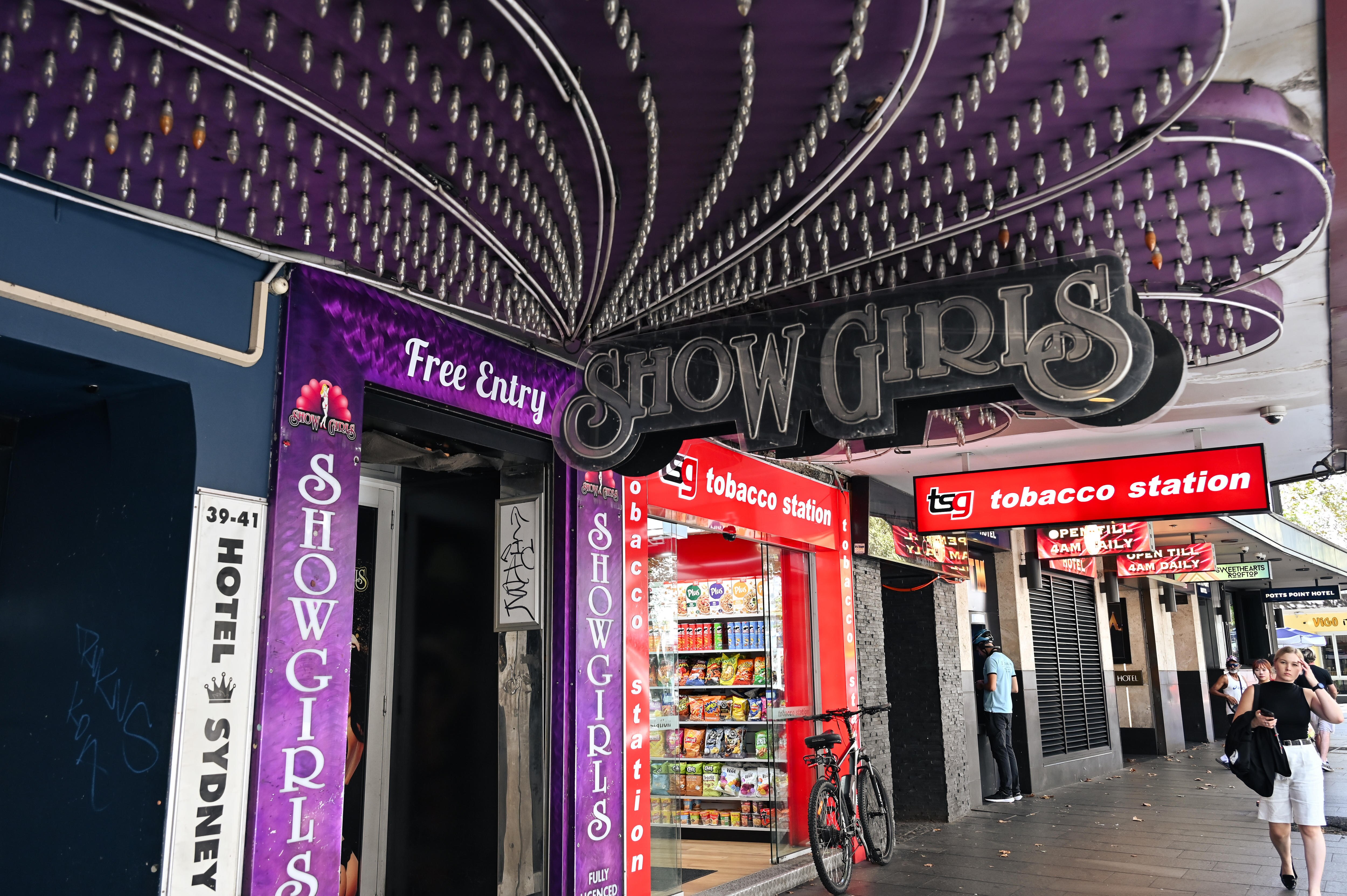 A purple sign with lights saying Showgirls in a shopping street.
