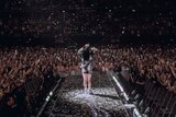 Billie Eilish stands at the end of a catwalk overlooking a packed arena audience