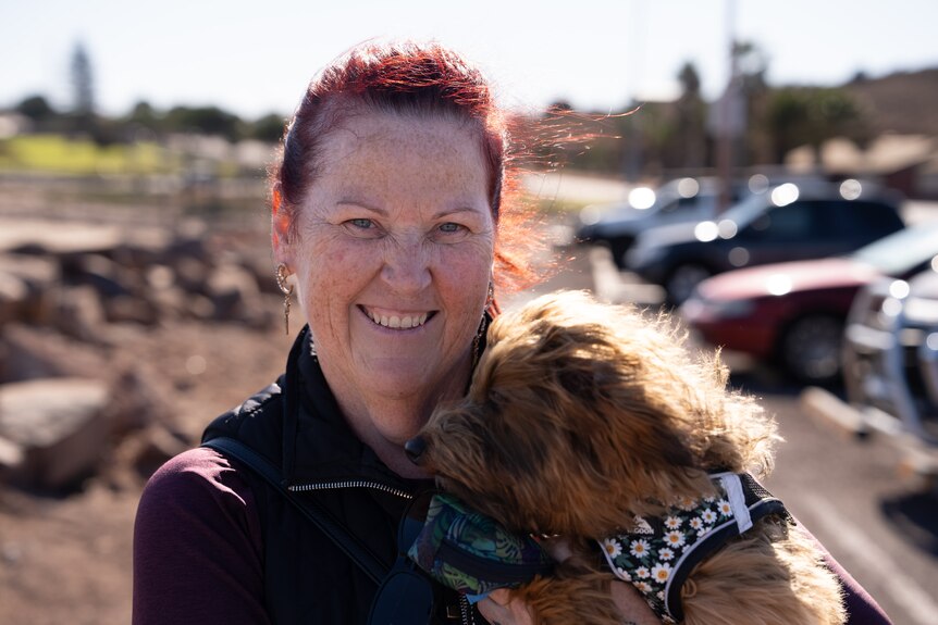 A woman smiles at the camera while cuddling her little dog close to her face.