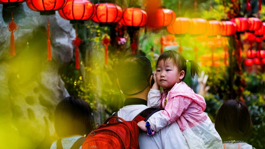 A little girl in her father's arms with a row of Chinese lanterns above them. 