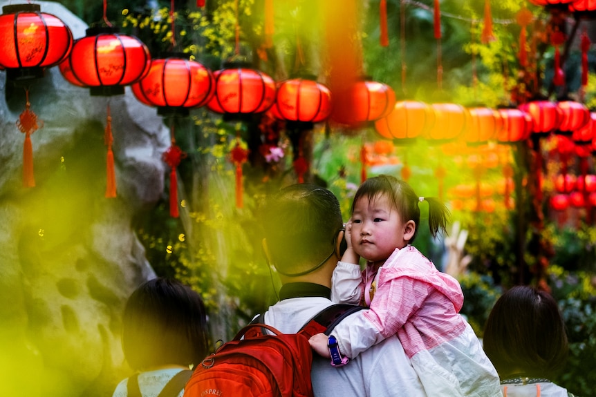 A little girl in her father's arms with a row of Chinese lanterns above them. 