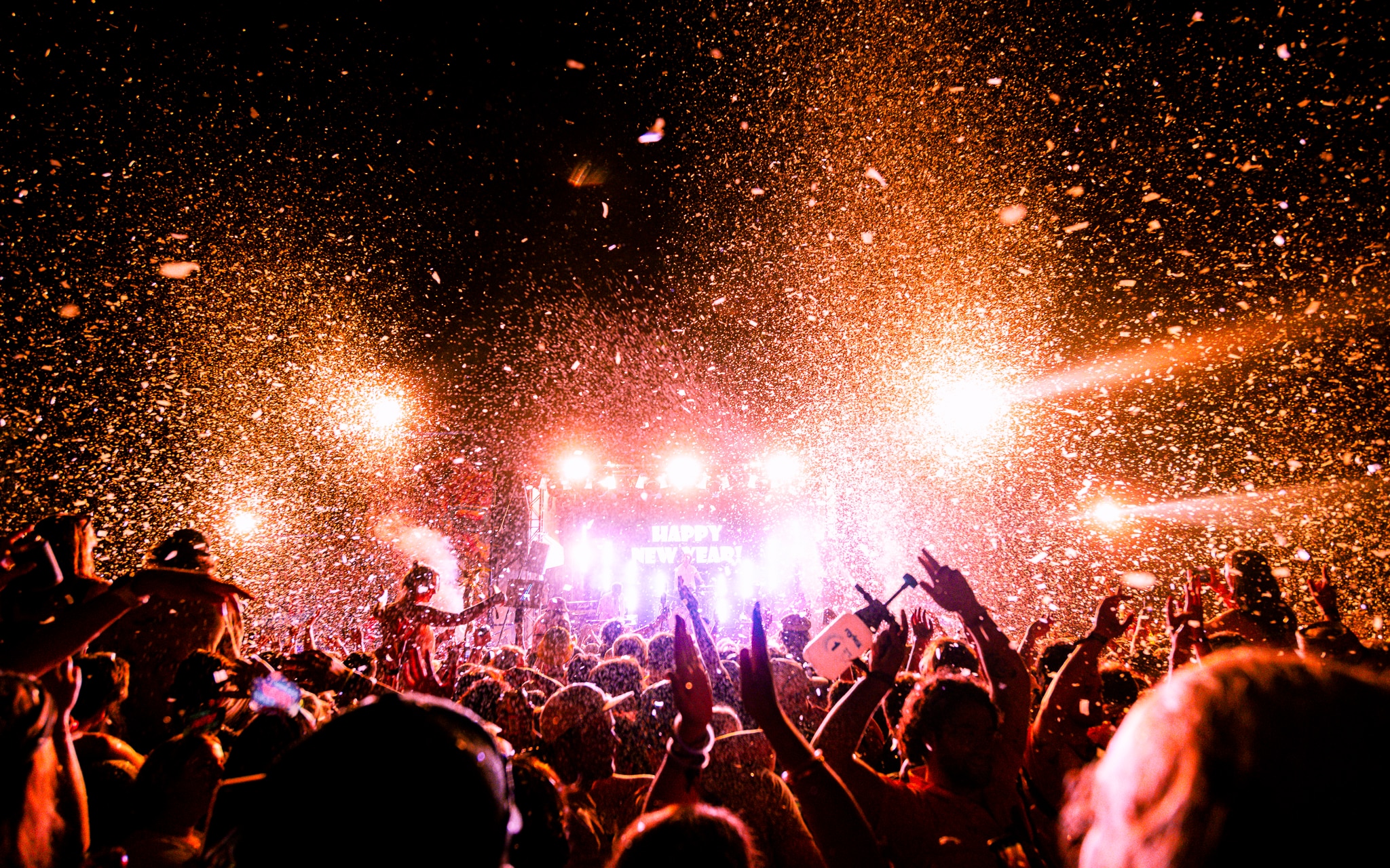 A festival crowd at night facing a lit up stage with a Happy New Year message on the stage screen