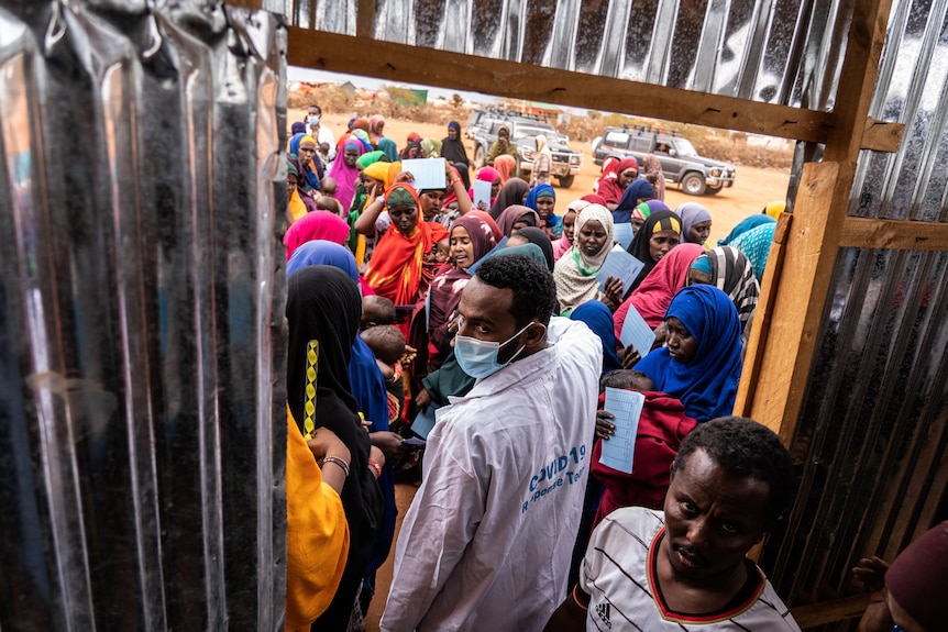 Health care workers gesture towards a crowd of people trying to get into the door of a clinic