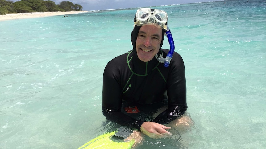 Ove sits in knee-deep water in a wet suit with his snorkel gear on his head.