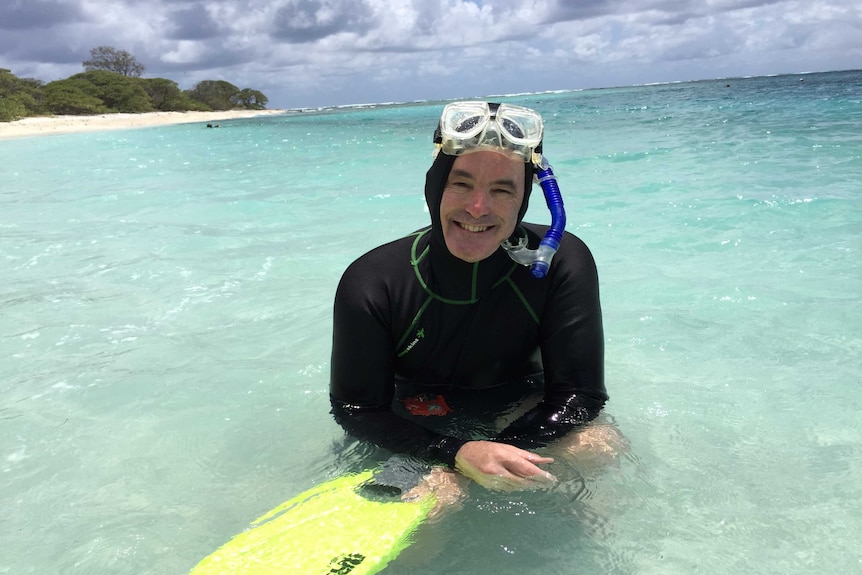 Ove sits in knee-deep water in a wet suit with his snorkel gear on his head.