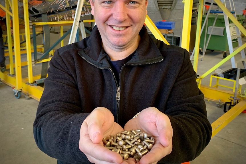 A man holds hundreds of rivets in his hands.
