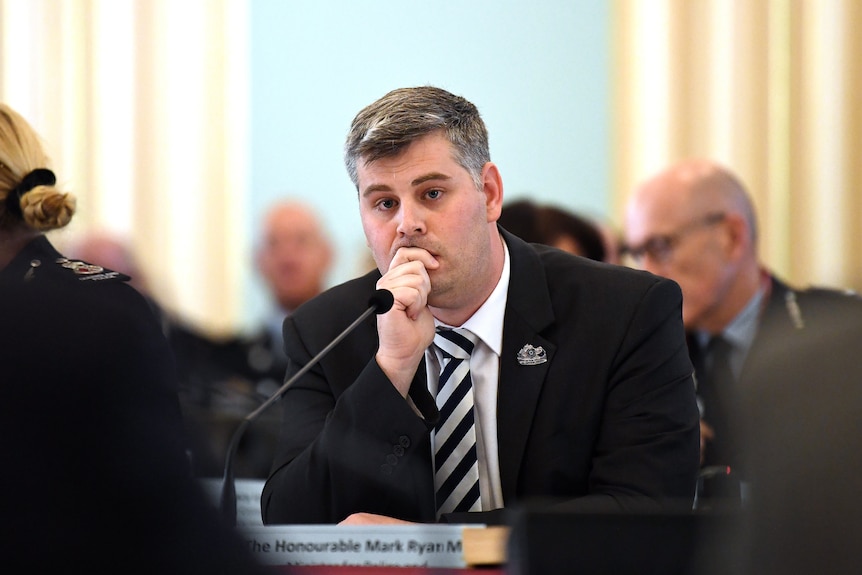 mark ryan sitting behind a desk during senate estimates leaning his head on his hand