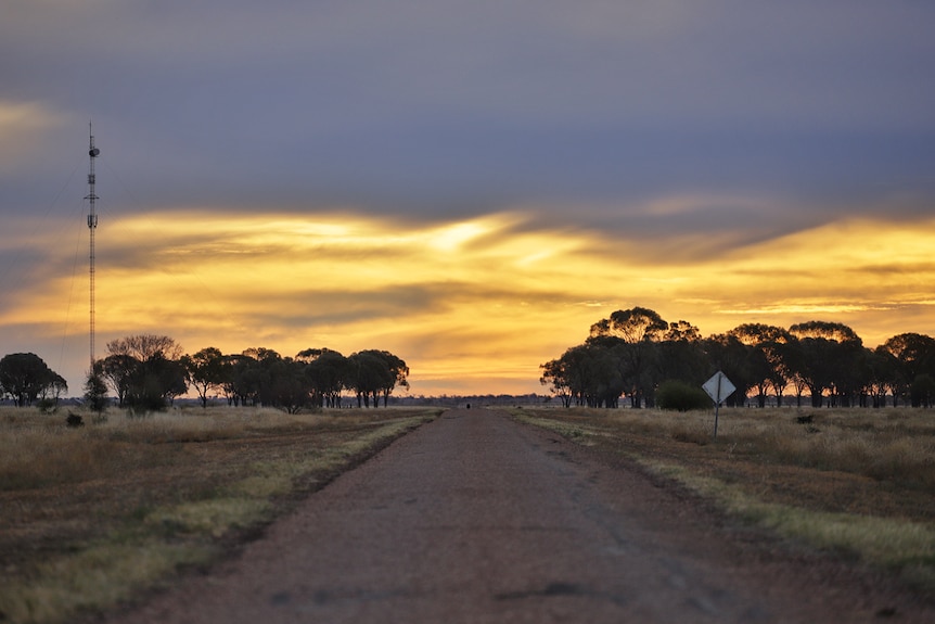 The sun sets over the a dirt road, with a radio tower alongside, at Barcaldine.