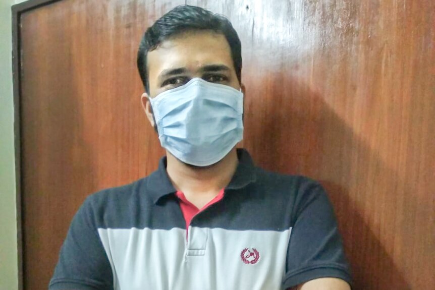 a man in a medical mask poses with his arms crossed.