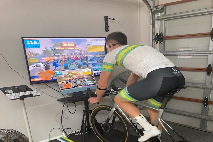 A man on a stationary bike set up in front of a laptop and TV screen